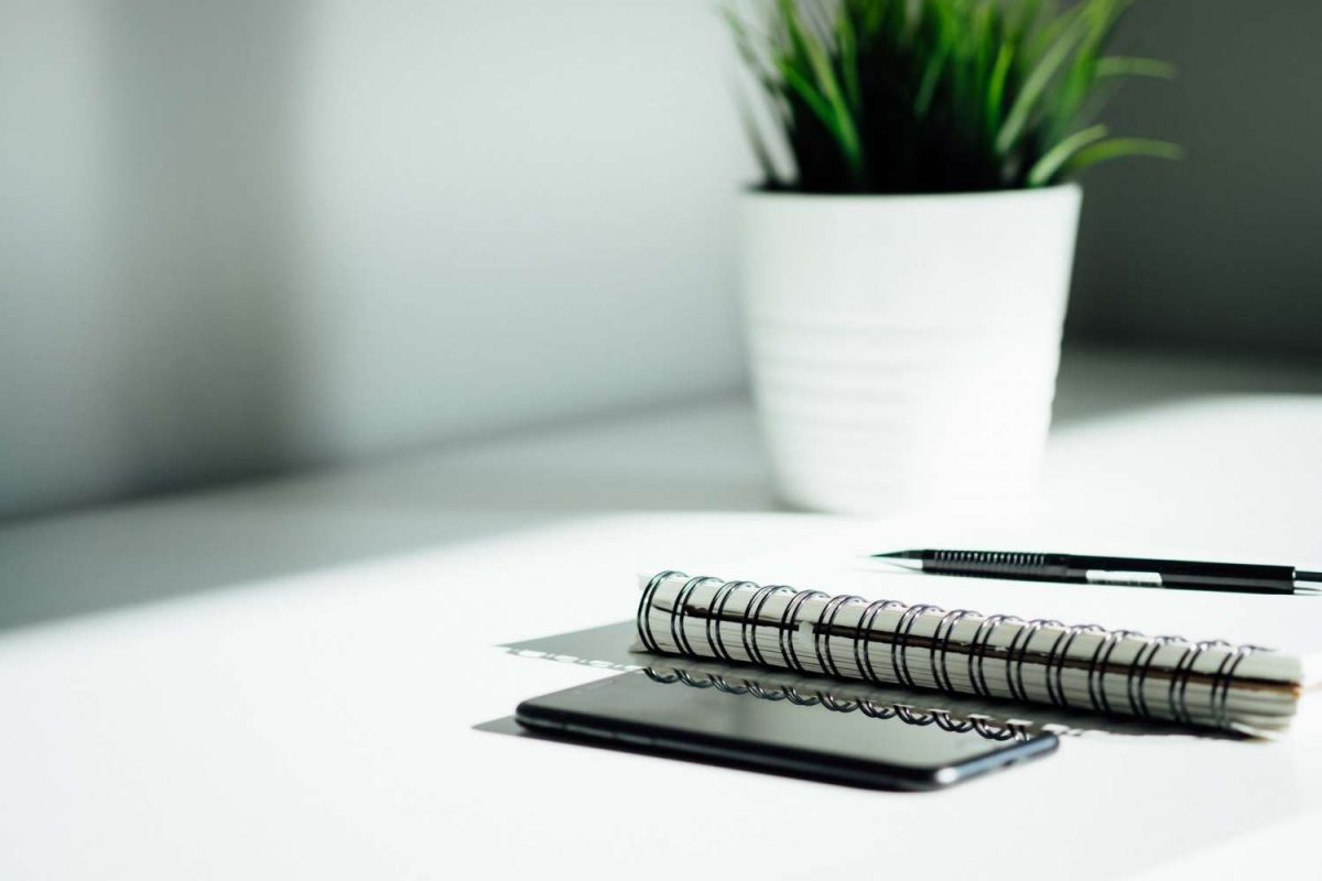 Cell phone, notebook, pencil and a small, white ceramic plant pot on the accounting office desk