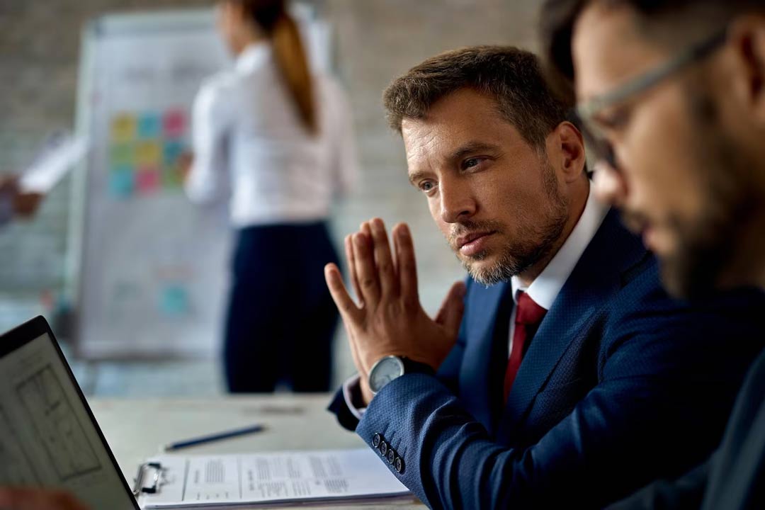 Dois executivos experientes, preocupados, sentados em mesa de escritório analisando dados do escritório