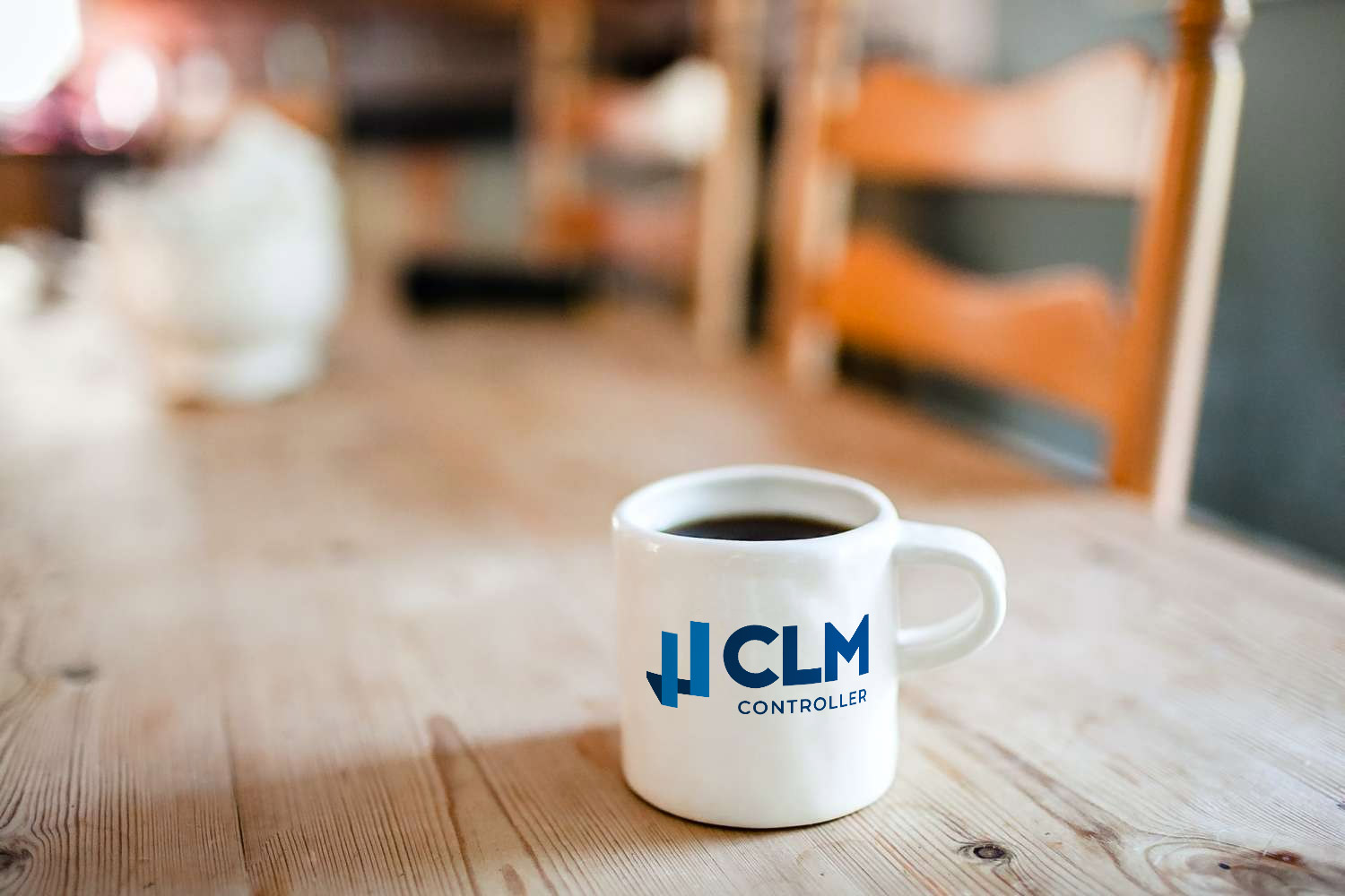 White ceramic coffee cup with CLM Controller logo on a table in the office