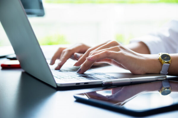 computer and cell phone on a table while a woman types about holdings